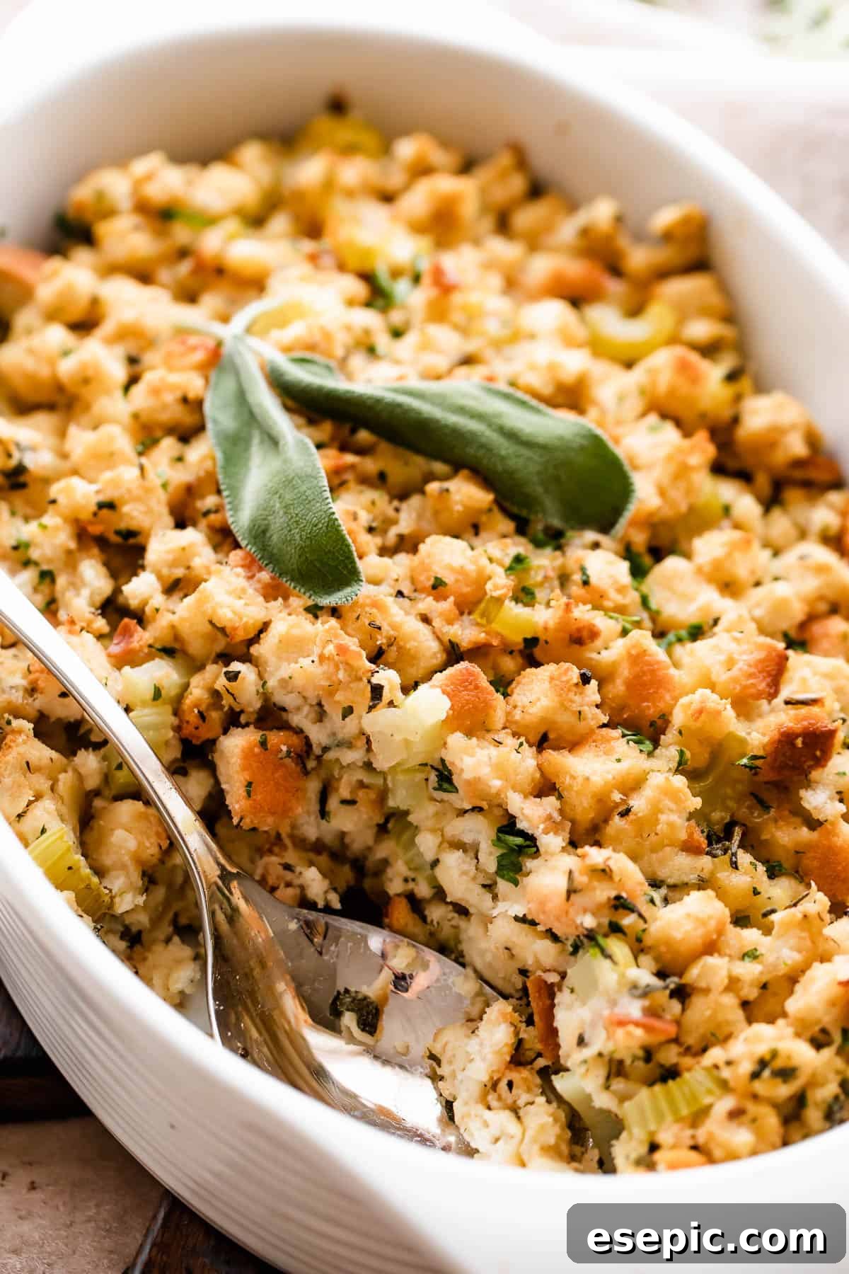 Savory Herb Stuffing Made Simple 2 An overhead shot of a scalloped casserole dish, filled with baked bread stuffing. A serving spoon is in the dish.
