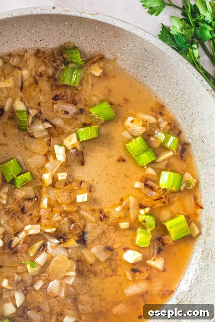 Savory Herb Stuffing Made Simple 5 A ceramic skillet with a mixture of chopped vegetables and wine.