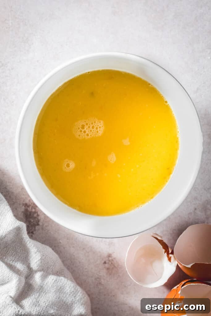 Savory Herb Stuffing Made Simple 6 A white mixing bowl with eggs and broth whisked together. Eggshells are nearby on the work surface.