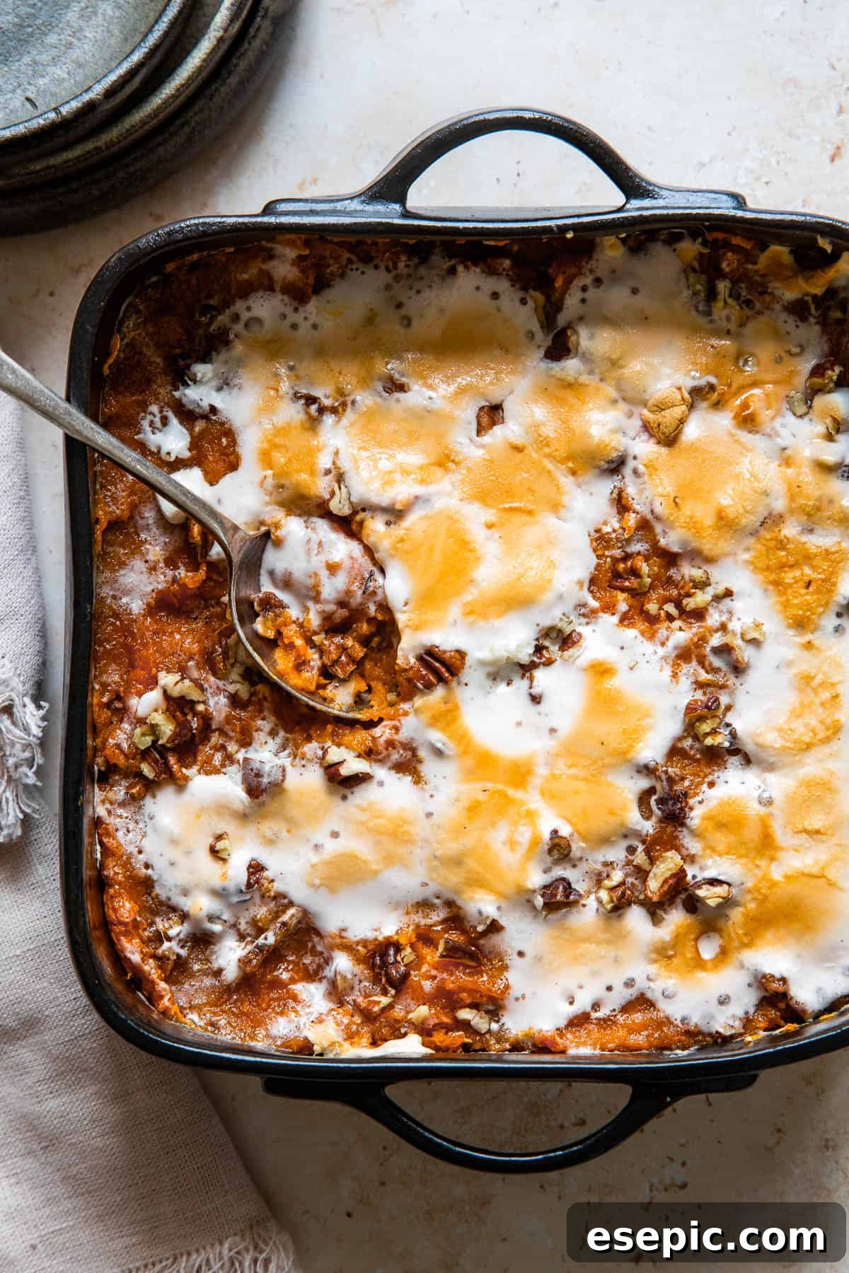 Golden Sweet Potato Delight 5 A serving spoon resting in a square black baking dish of sweet potato casserole, with the golden-brown marshmallow topping visible.