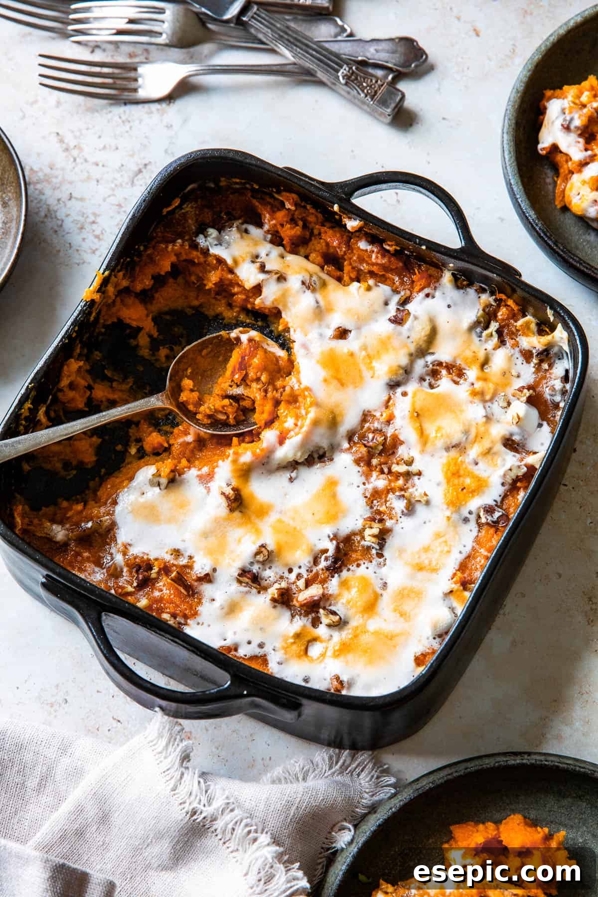 Golden Sweet Potato Perfection 7 A square black baking dish filled with sweet potato casserole, topped with beautifully melted, golden-brown marshmallows. Several portions have been scooped out, revealing the creamy interior of the dish.