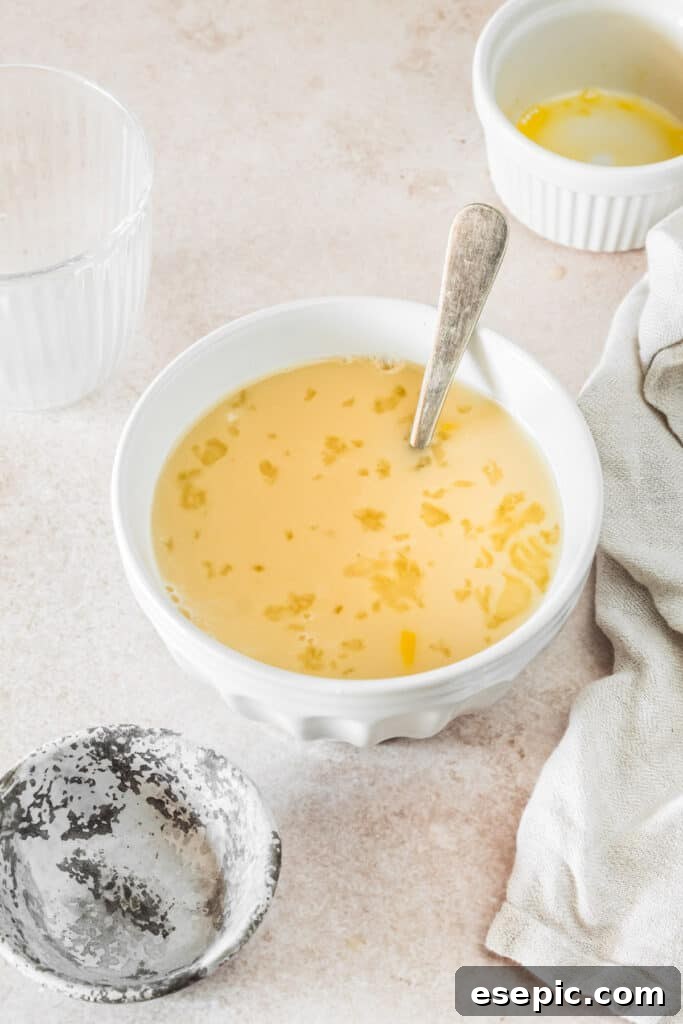 A small mixing bowl with egg, milk, activated yeast, and water gently mixed together. A floury spoon and a dish towel are visible on the work surface, ready for the next steps.