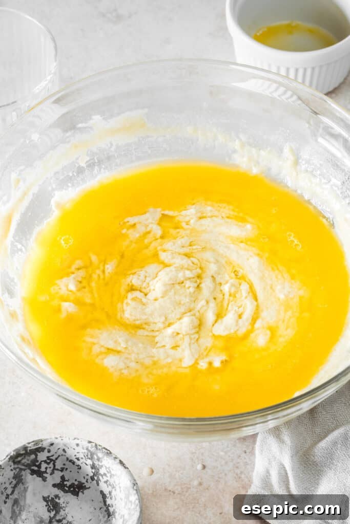 A large mixing bowl containing soft, sticky dough with melted butter being poured in, ready for final mixing.