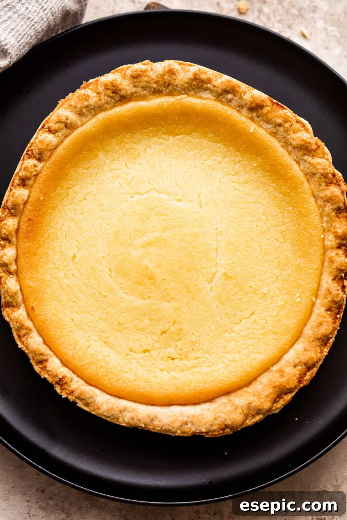 Overhead shot of a meticulously homemade buttermilk pie resting on a sleek black plate, ready for serving.