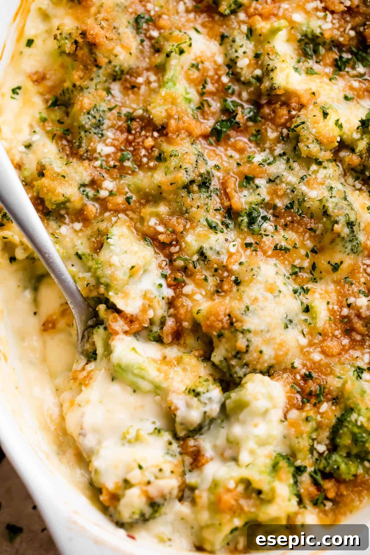 A tantalizing overhead view of an oval baking dish filled with Creamy Cheesy Broccoli Casserole, with a serving spoon creating a swirl through the golden-brown topping and rich, bubbly sauce.