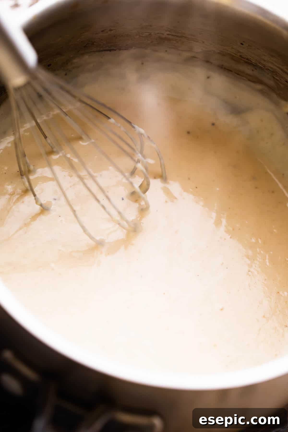 Velvety Creamy Chicken Soup 4 A close-up shot of a saucepan on a stovetop, with a whisk actively mixing ingredients to create homemade cream of chicken soup.