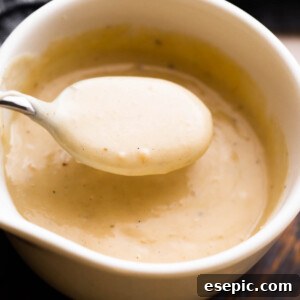 A close-up, inviting overhead shot of a white ceramic cup filled with homemade cream of chicken soup, with a spoon gently scooping a portion, highlighting its luscious texture.