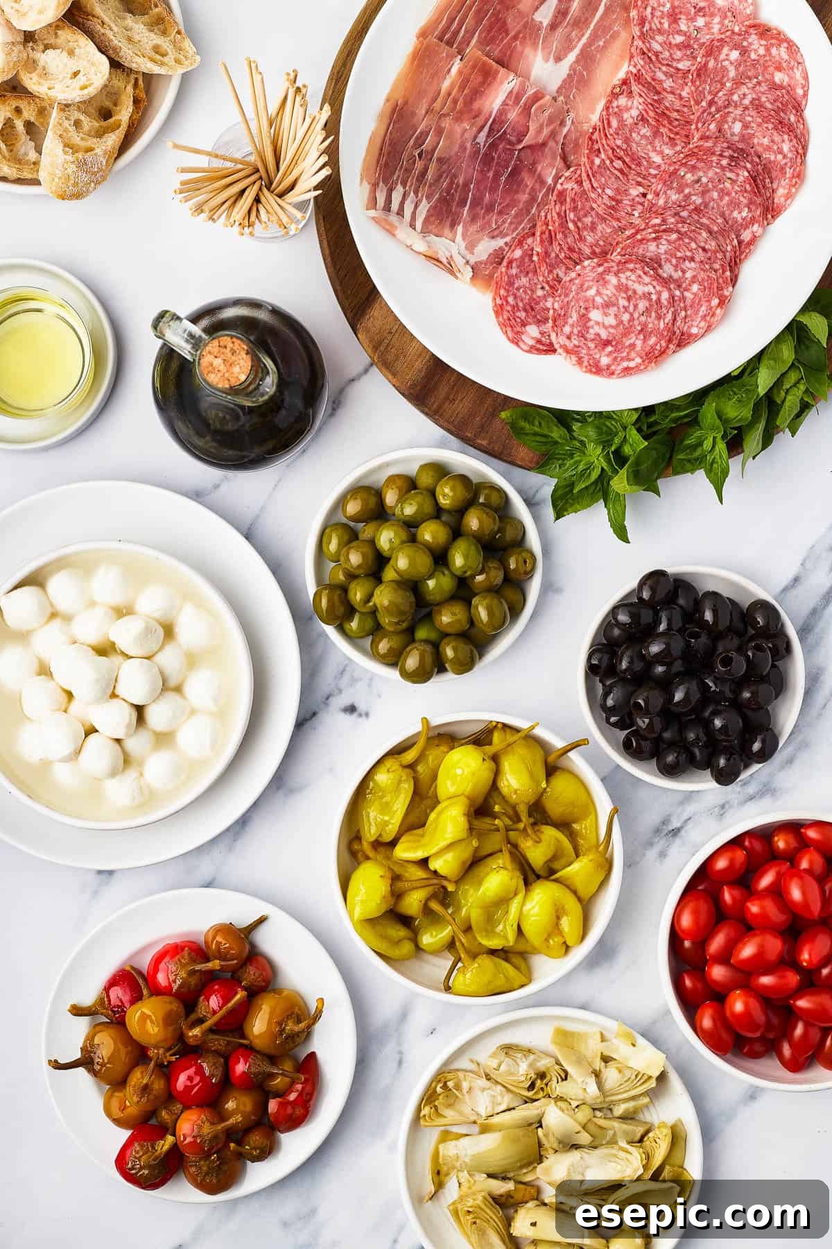 Mini skewers loaded with salami, olives, peppers, and more are stacked and shaped in a ring to make this easy Holiday Antipasto Wreath! Clockwise from top: Salami and prosciutto slices, green olives, black olives, grape tomatoes, artichoke hearts, pepperoncini, sweet cherry peppers, mozzarella balls, balsamic vinegar, oil, sliced bread.