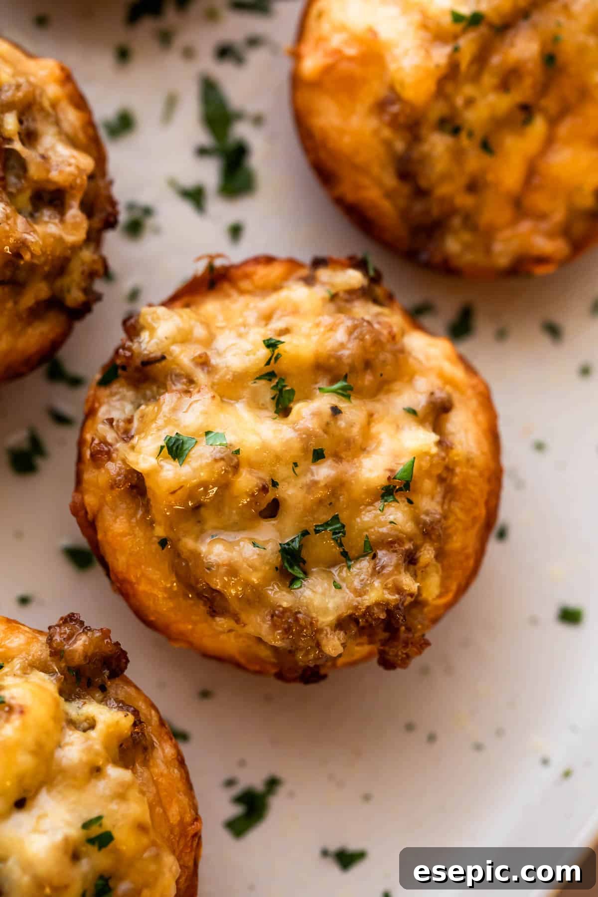 These breakfast egg cups are the perfect grab-and-go option! Italian sausage and scrambled eggs are topped with cheese and baked in a biscuit crust. Close-up overhead shot of a single baked breakfast egg cup set on a serving plate, garnished with parsley.