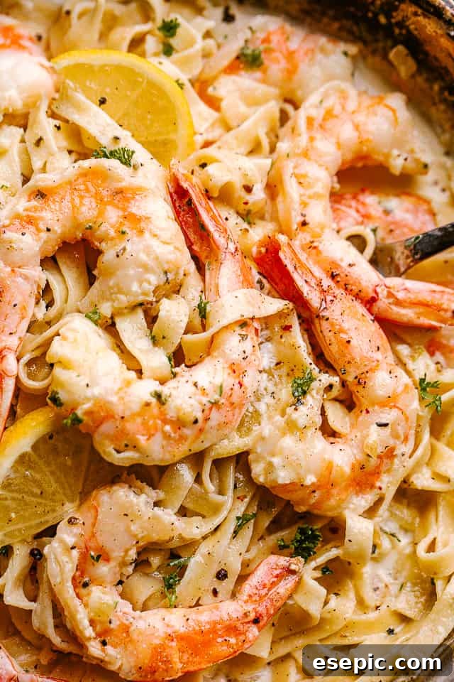 Creamy Shrimp Alfredo Pasta: Quick and Delicious! Close-up of creamy shrimp Alfredo pasta in a deep pan, garnished with fresh lemon slices and parsley.