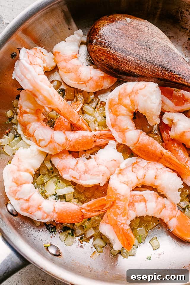 Decadent Shrimp Alfredo Delight 2 Shrimp cooking in a pan with minced garlic and herbs, releasing a delicious aroma.
