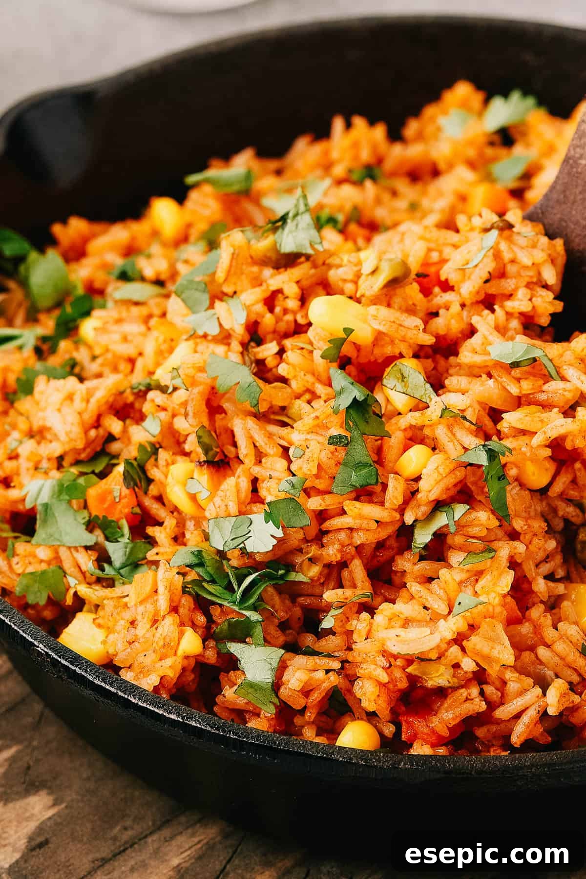 Side view of Mexican rice in a cast iron skillet, with a wooden utensil in the pan.