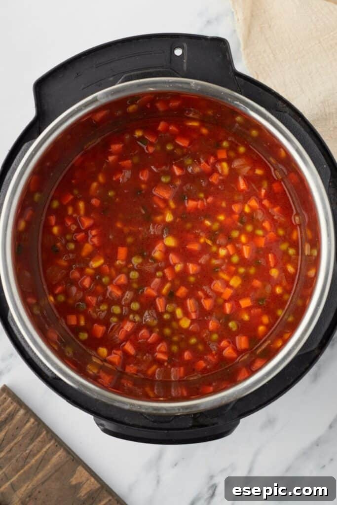 Speedy Instant Pot Mexican Rice 7 Overhead shot of an Instant Pot, with vegetables and a tomato-based broth inside.