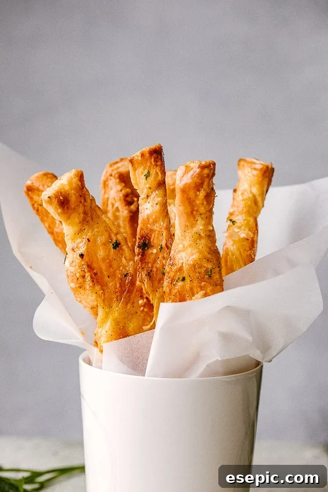 Golden brown puff pastry cheese sticks arranged neatly in a white serving cup, ready to be enjoyed.