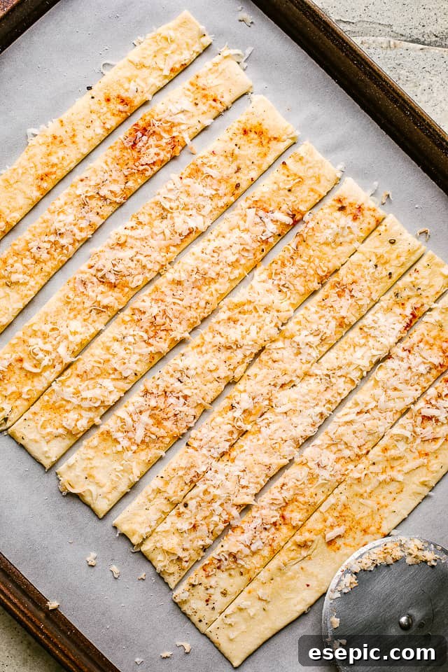 Seasoned and cheesed puff pastry dough meticulously sliced into even strips with a pizza cutter.