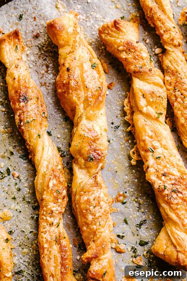 Freshly baked puff pastry cheese sticks cooling on a parchment-lined baking sheet, showing their golden crust.