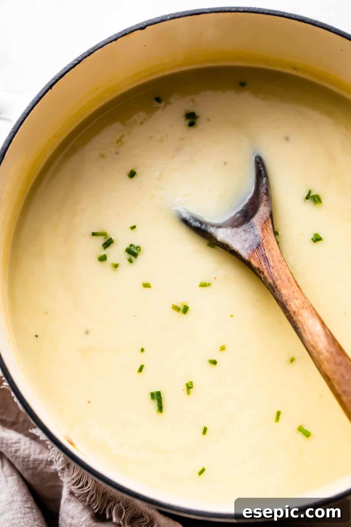 overhead shot of wooden spoon stirring through leek and potato soup in a dutch oven.