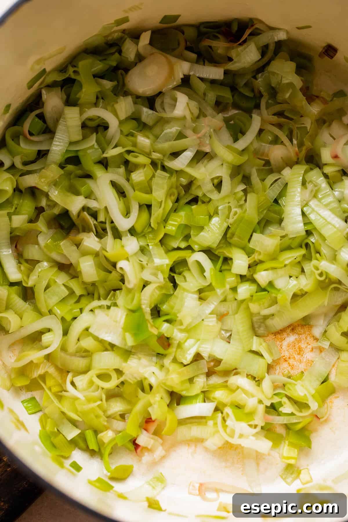 frying sliced leeks in a white dutch oven.