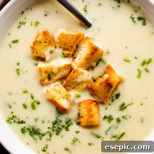 overhead close up shot of leek and potato soup served in a white bowl and garnished with croutons and chopped chives.