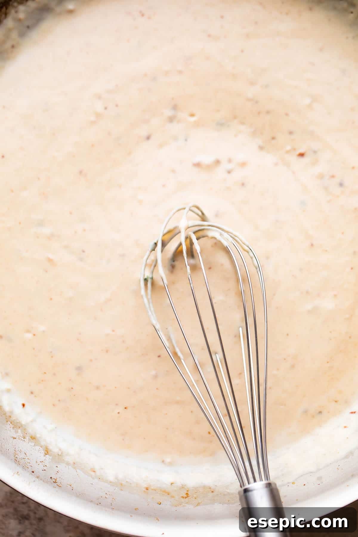 Velvety Parmesan Gnocchi with Succulent Shrimp 5 whisking through white cream sauce in a skillet.