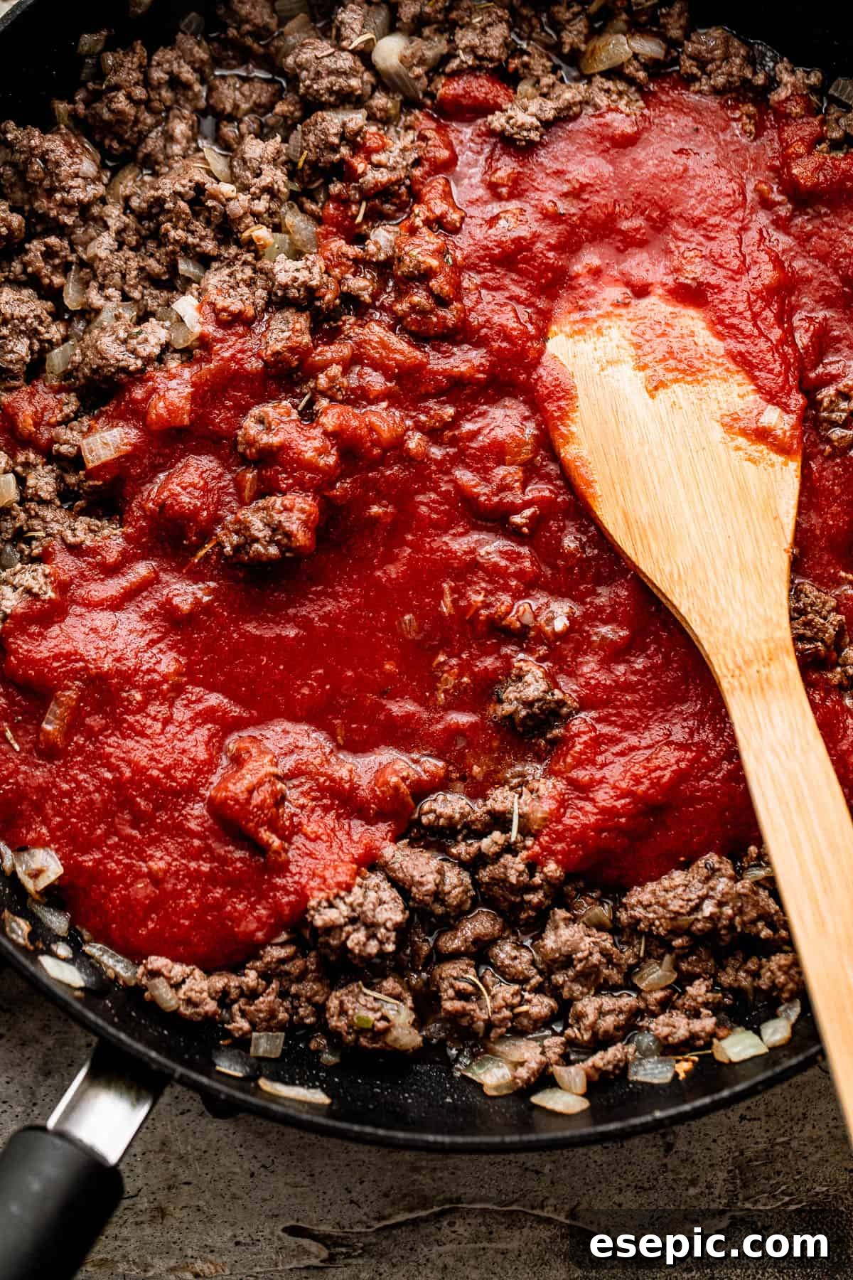 cooking ground beef with tomato sauce in a skillet.