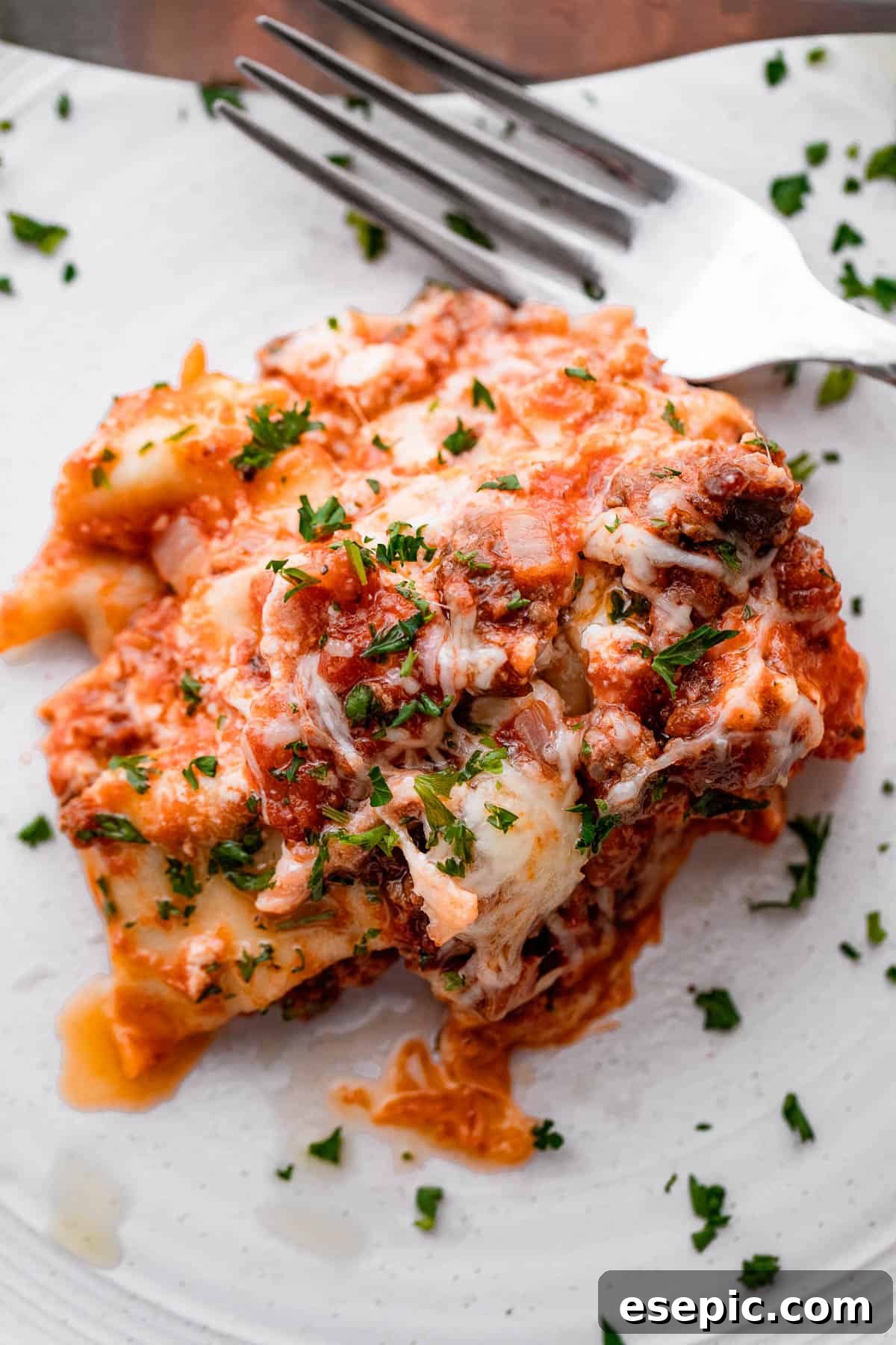 piece of lasagna served on a white plate with a fork placed to the side of it.