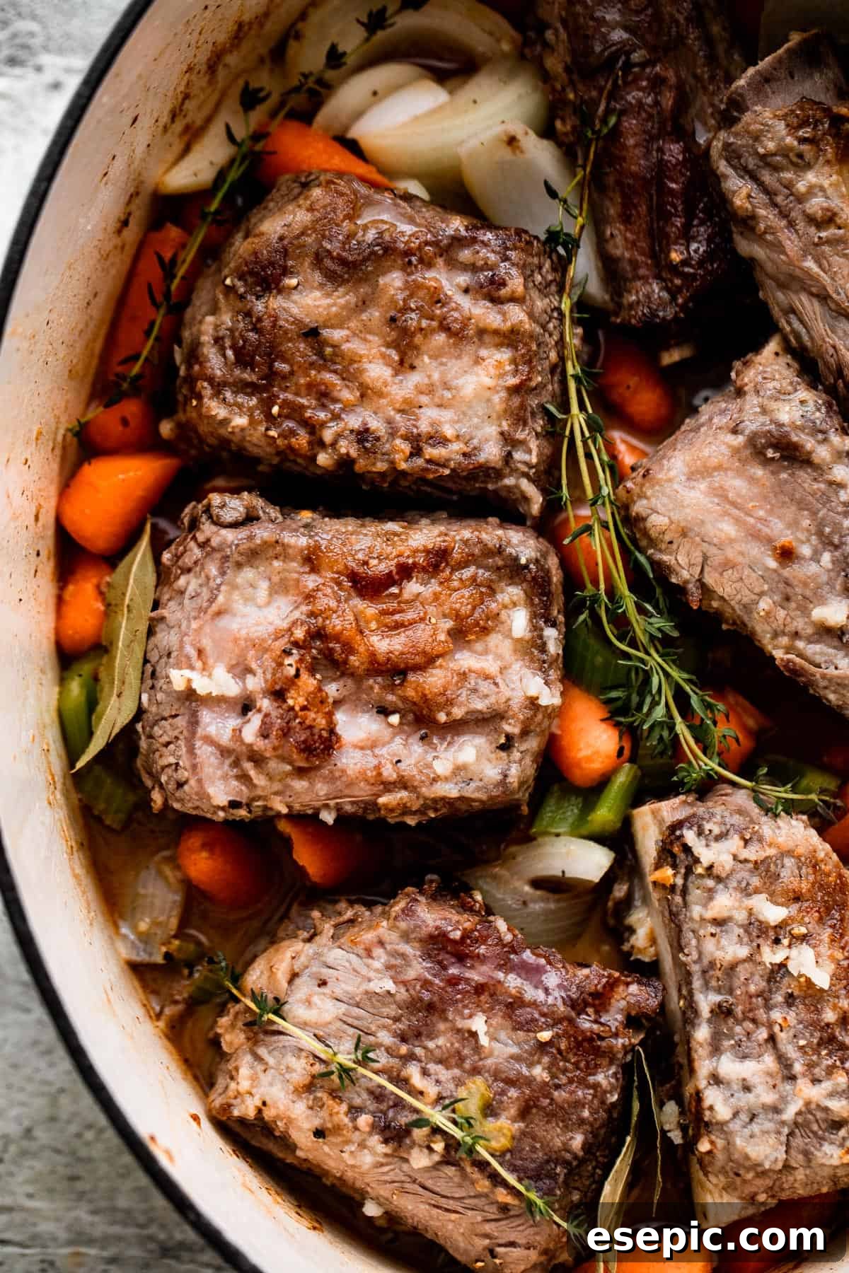 Fall-Off-The-Bone Slow Cooker Short Ribs 5 carrots, onions, thyme sprigs, and beef short ribs arranged inside the slow cooker insert.