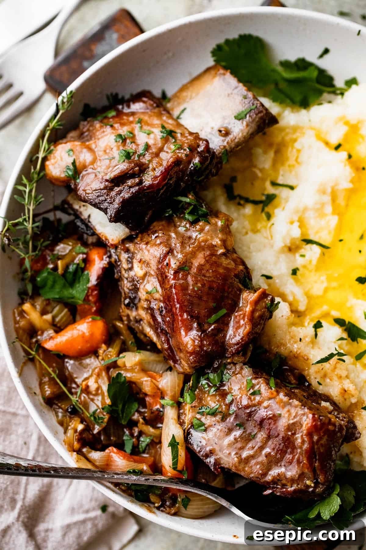 close up shot of a dinner plate with three short ribs arranged around mashed potatoes, with veggies and onions set on the other side of the short ribs.