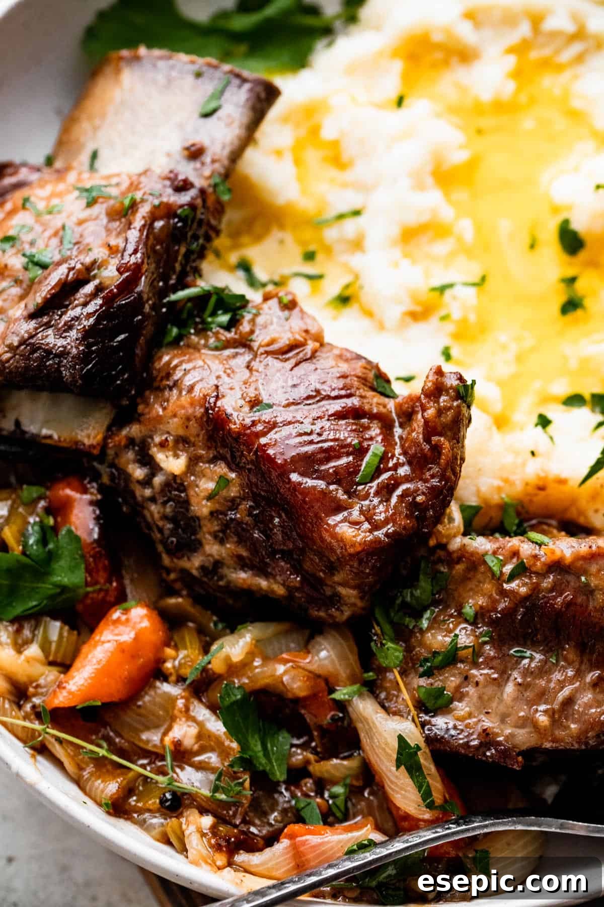 close up shot of a dinner plate with three short ribs arranged around mashed potatoes, with veggies and onions set on the other side of the short ribs.