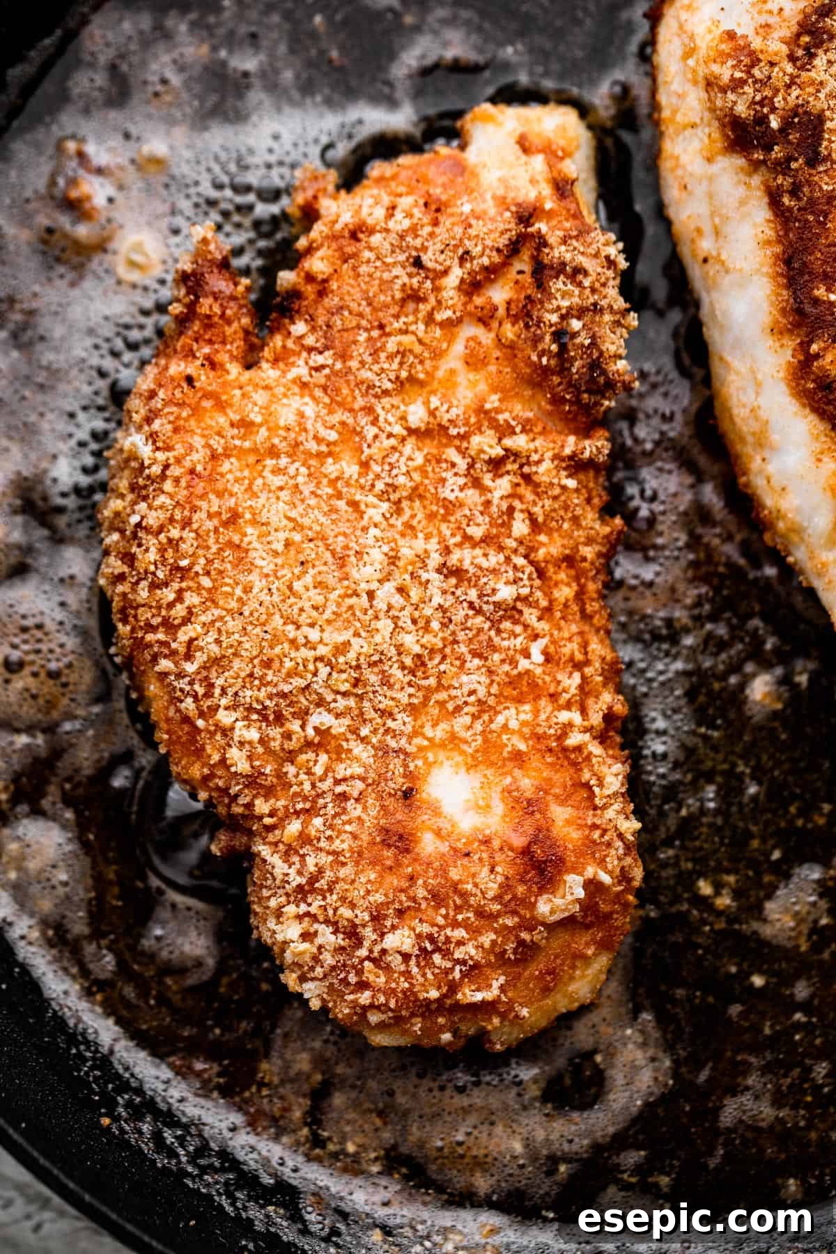 Perfectly Crispy Chicken Schnitzel 5 overhead shot of breaded chicken frying in a black skillet.