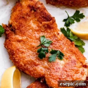 Perfectly Crispy Chicken Schnitzel 8 up close shot of chicken schnitzel garnished with parsley and lemon wedges placed around the chicken.