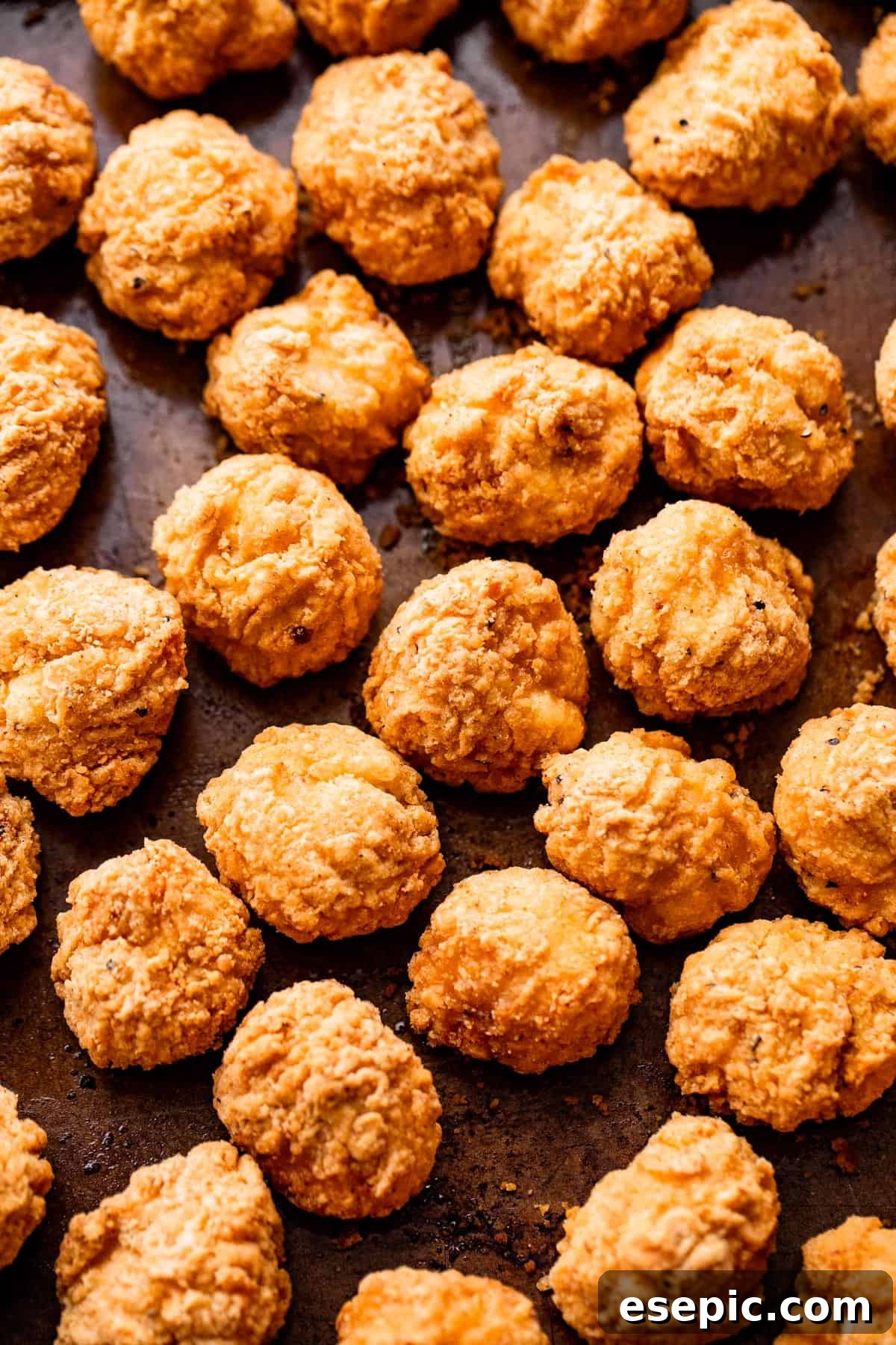 Breaded popcorn chicken pieces arranged neatly on a sheet pan, ready for cooking.