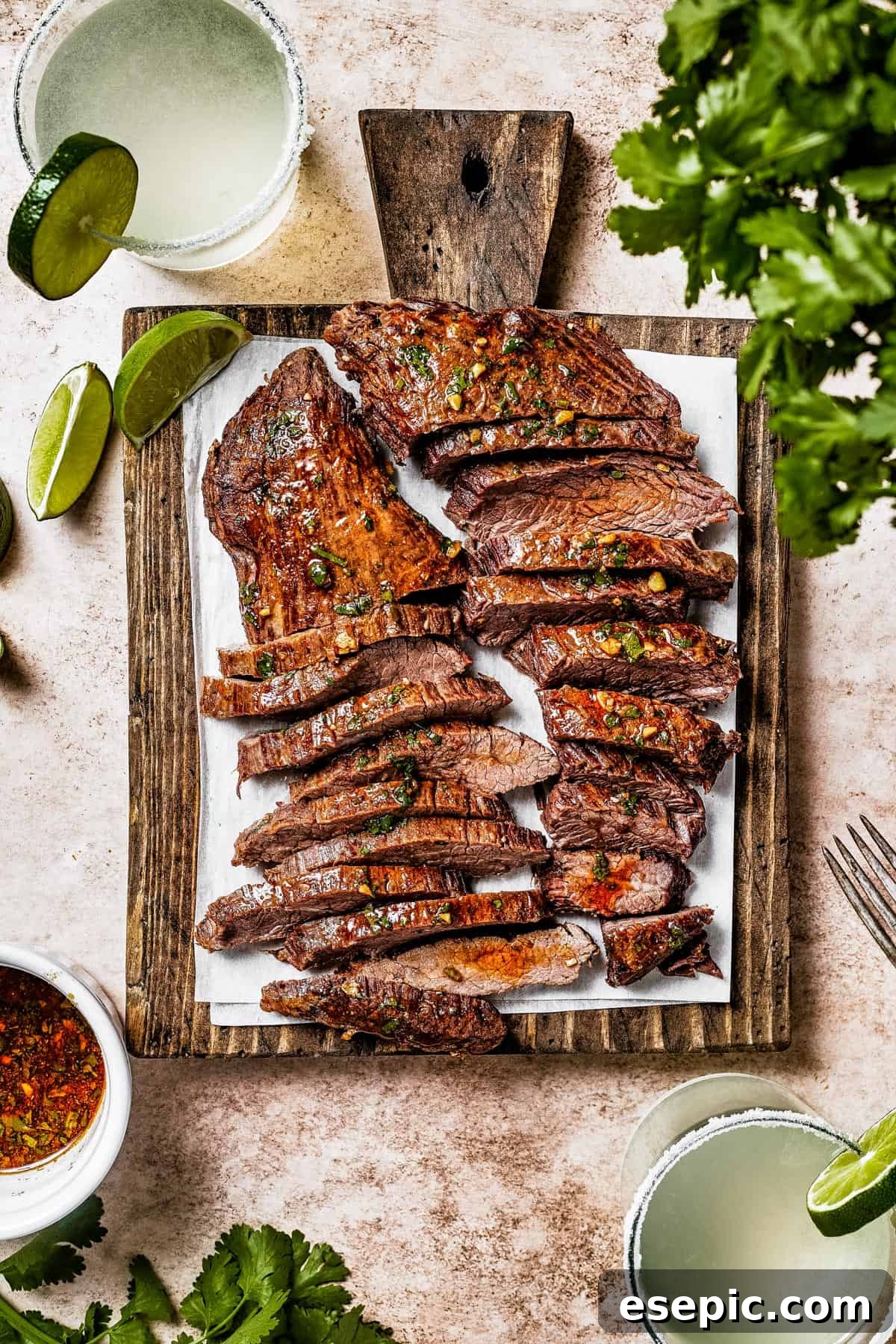 A cutting board with thinly sliced flank steak, surrounded by fresh limes and cilantro.