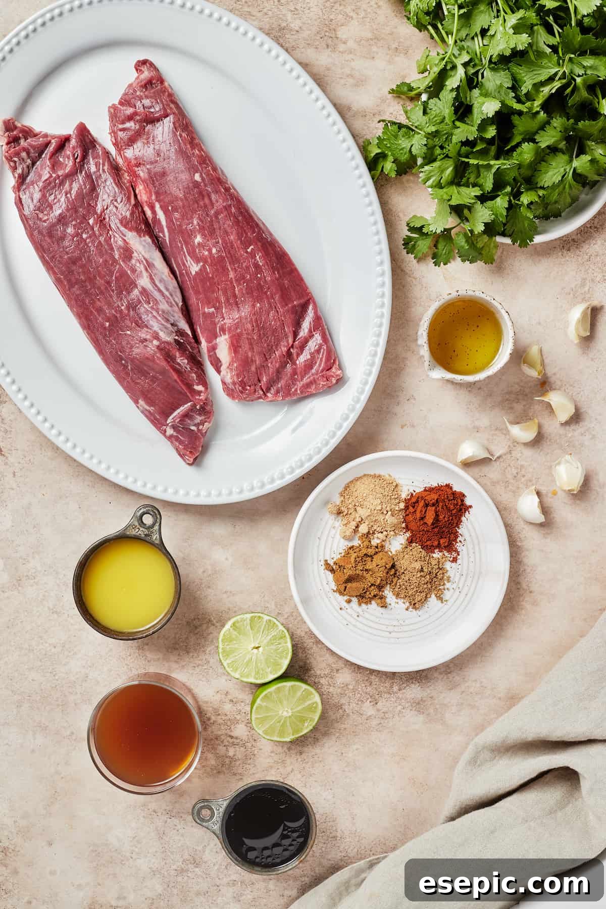 A flat lay of all ingredients for Instant Pot Carne Asada: flank steak, fresh cilantro, avocado oil, minced garlic, a mix of spices, lime and orange halves, tamari sauce, and beef broth.
