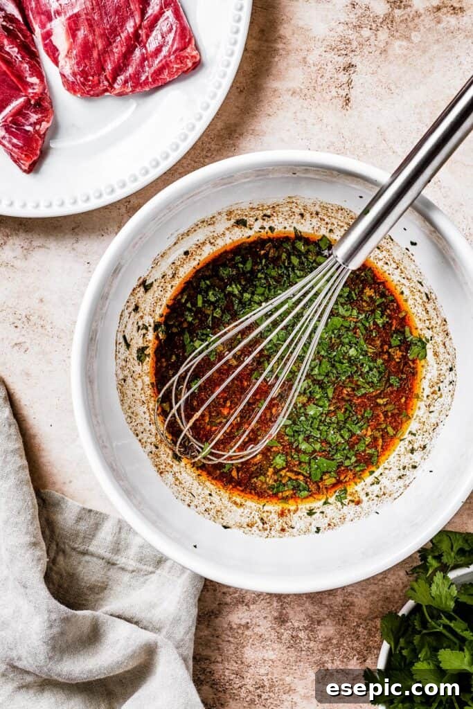A white mixing bowl with dark-brown marinade and a whisk resting in it, showing the marinade preparation.