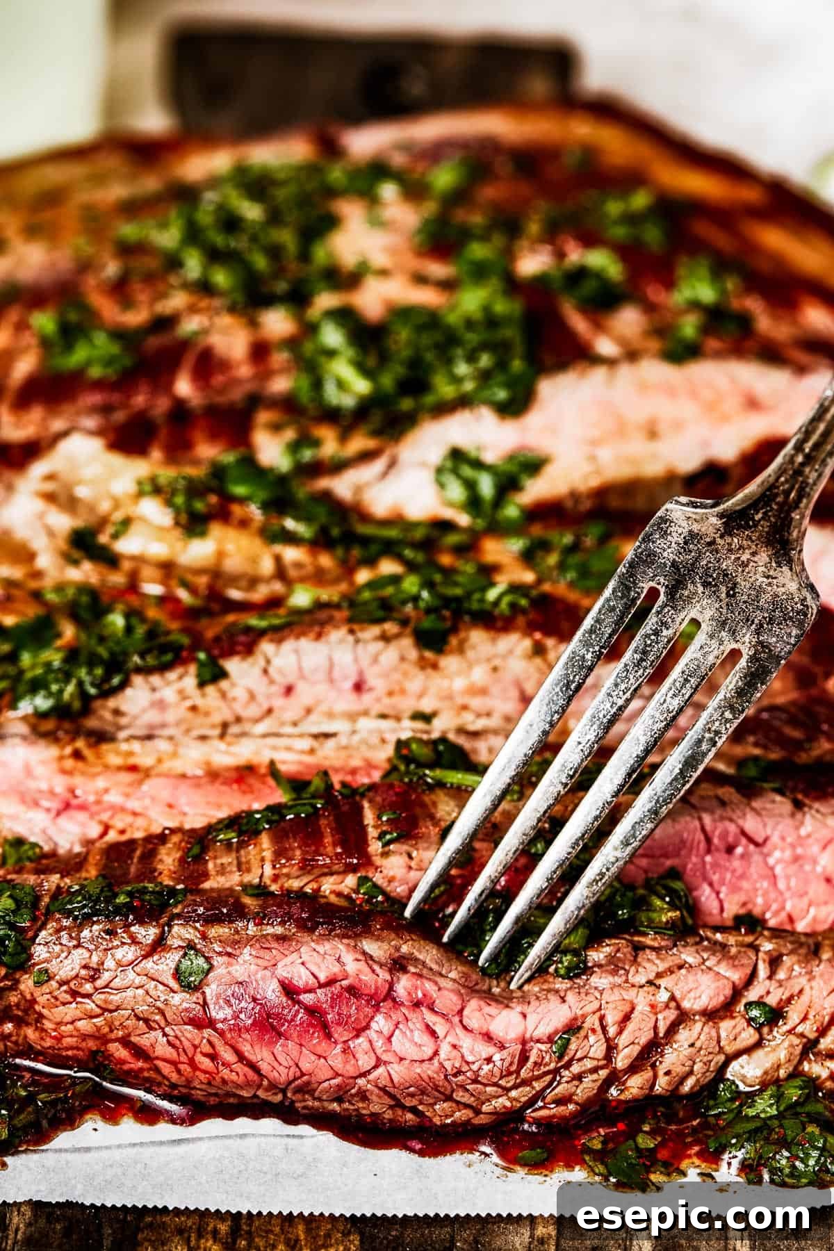 A close-up side view of perfectly sliced, tender flank steak on a cutting board, with a fork piercing a piece.
