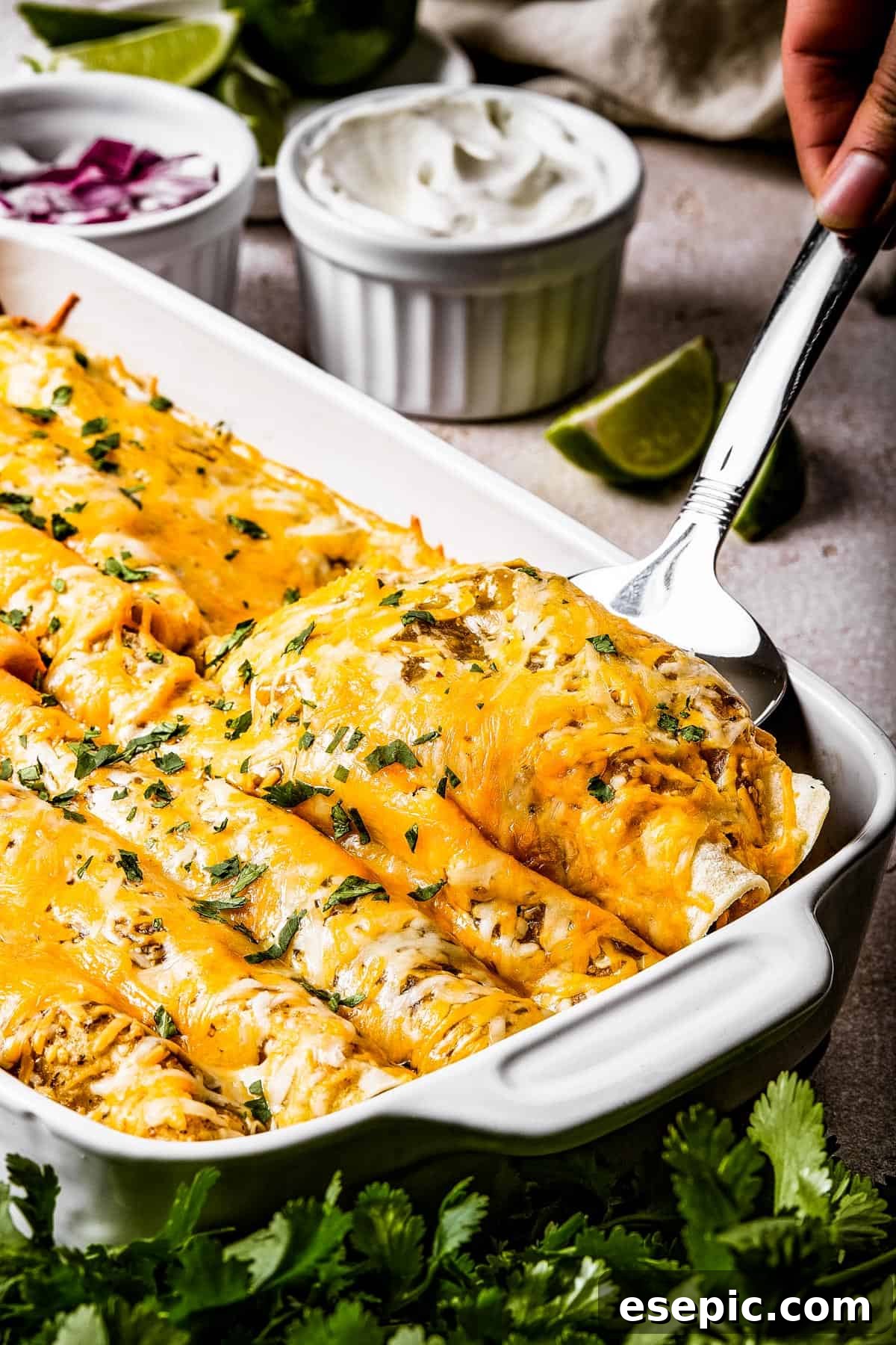 Tangy Tomatillo Chicken Enchiladas 3 A silver spoon is lifting two enchiladas from a white baking dish.