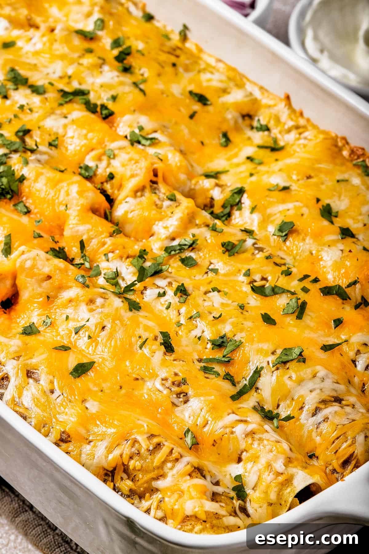 Tangy Tomatillo Chicken Enchiladas 9 Close-up of a baking dish of cheesy enchiladas, sprinkled with fresh herbs.