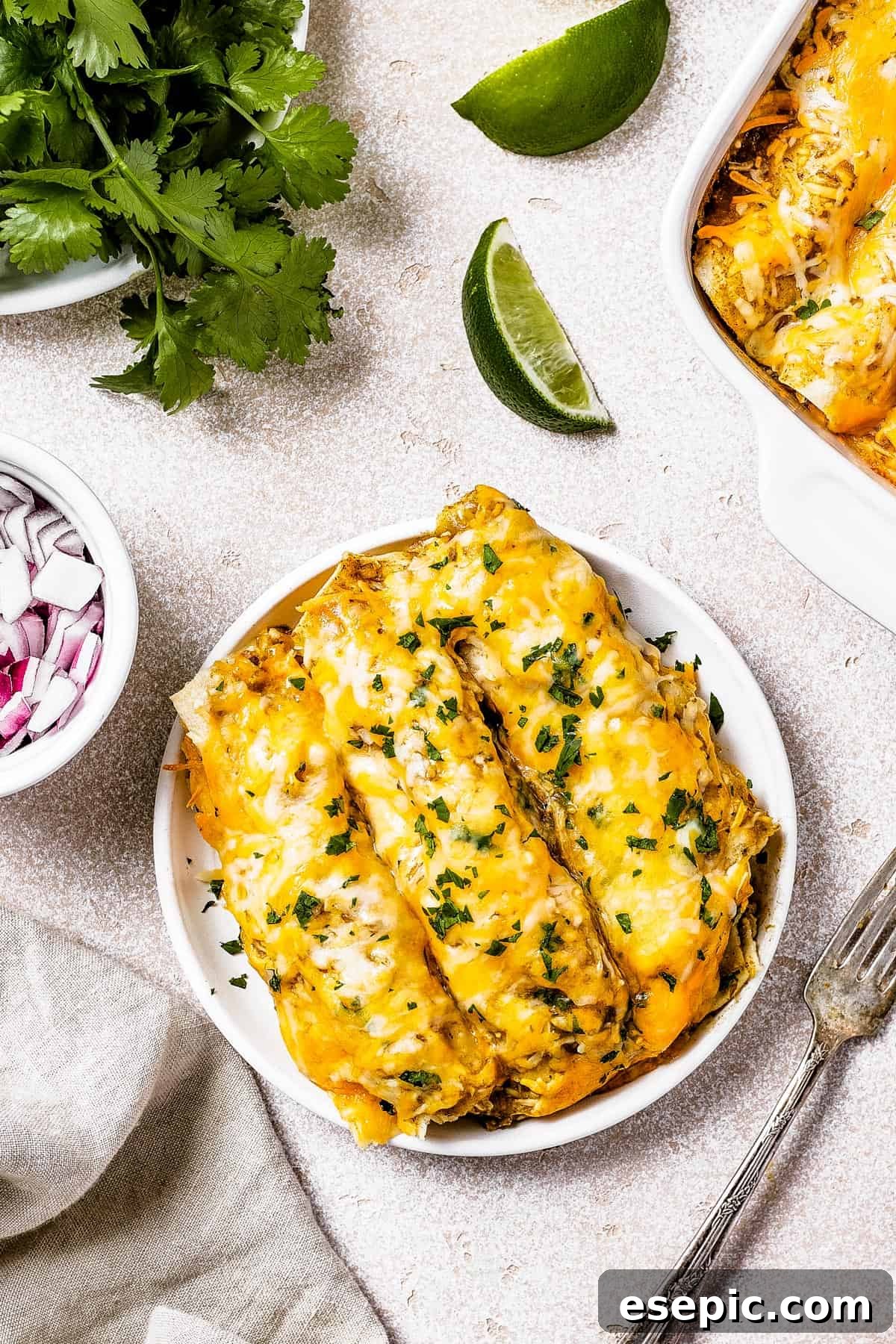 Tangy Tomatillo Chicken Enchiladas 10 A serving of chicken enchiladas on a small white plate, net to a dish of chopped onion and a dish of fresh cilantro.