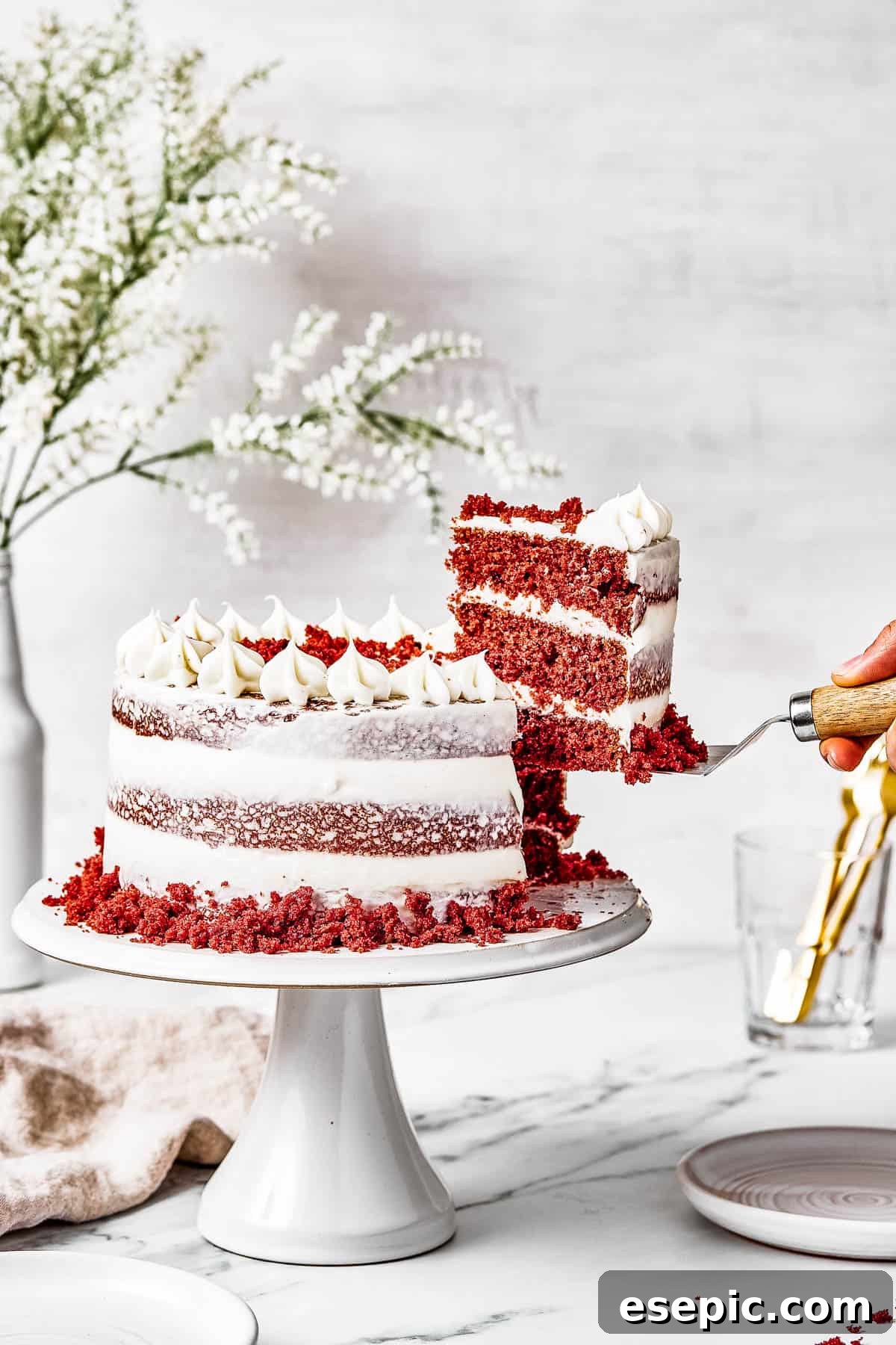 Decadent Red Velvet Dream 2 A woman's hand is lifting a perfect slice of homemade Red Velvet Cake on a serving utensil, showcasing the vibrant red layers and creamy white frosting.