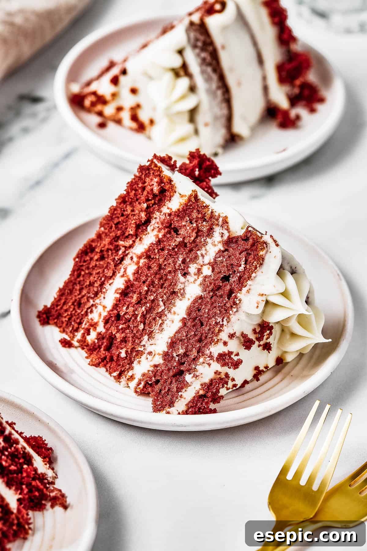 Decadent Red Velvet Dream 10 A delicious slice of Red Velvet Cake served on a small white plate, accompanied by golden forks on the table, highlighting its elegance.