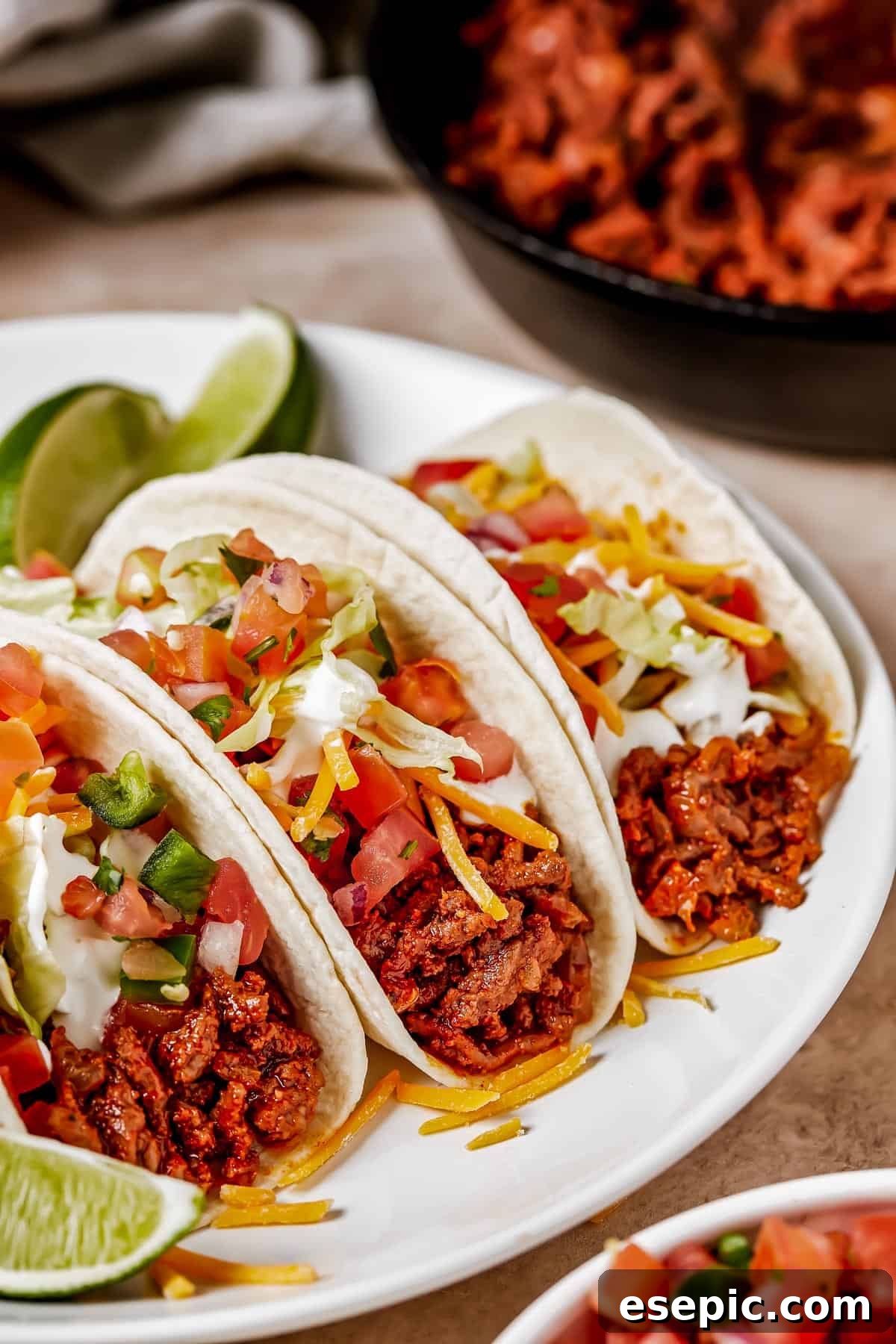 Quick and Flavorful Ground Beef Tacos 3 Three soft tacos on a plate with lime wedges.