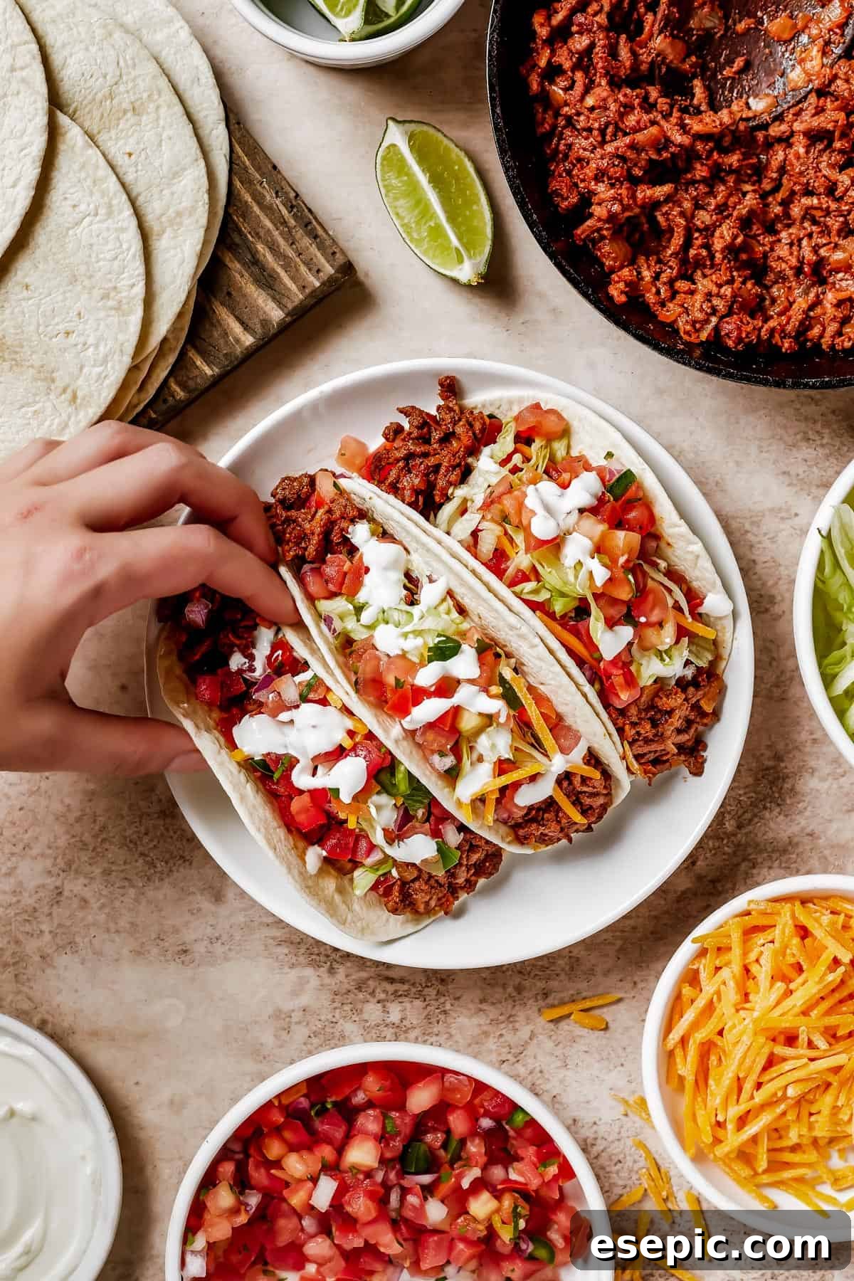 Quick and Flavorful Ground Beef Tacos 7 A woman's hand lifts a soft taco off of a plate.