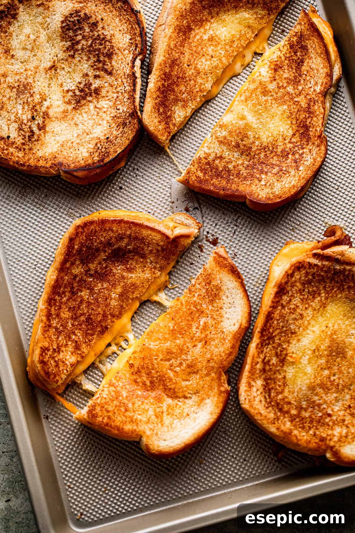 Golden Oven Baked Cheese Melts 2 Four baked grilled cheese sandwiches set on a baking sheet and diagonally cut in half, showcasing melted cheese.
