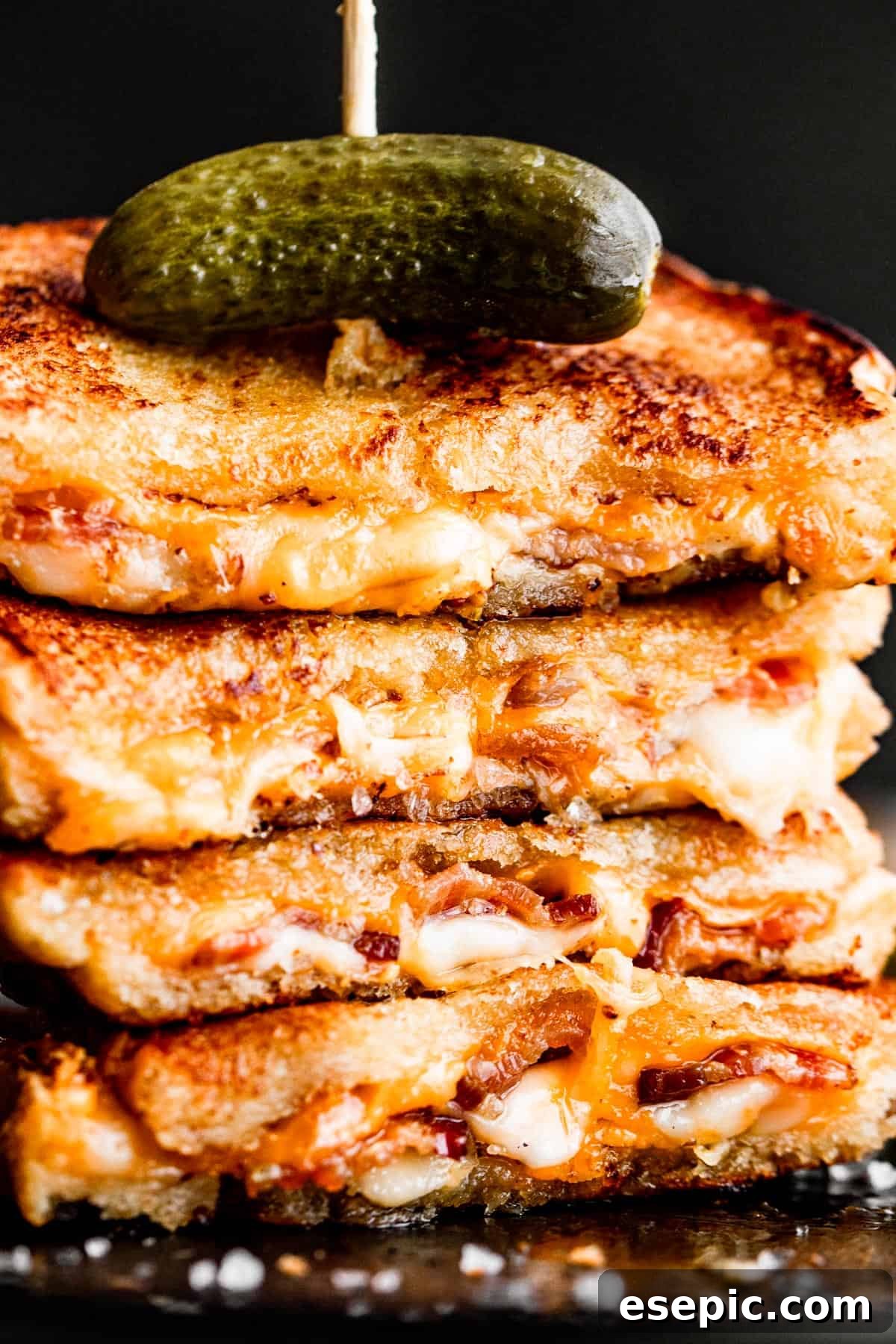 Golden Oven Baked Cheese Melts 3 A stack of golden baked grilled cheese sandwiches, topped with a pickle spear and held together with a long toothpick.
