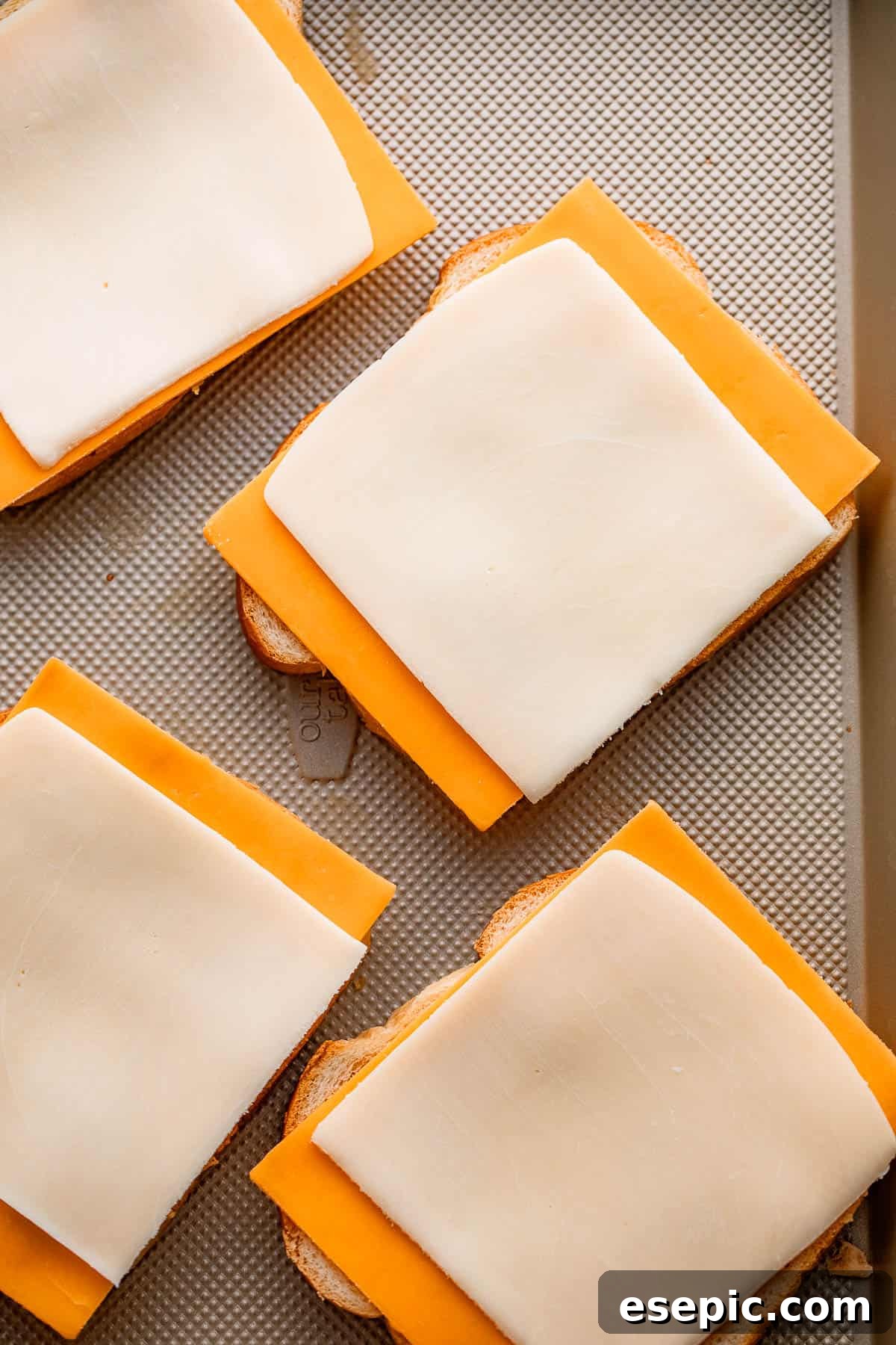Golden Oven Baked Cheese Melts 5 Slices of mozzarella and sharp cheddar cheese carefully placed on four bread slices, ready to be assembled into sandwiches.