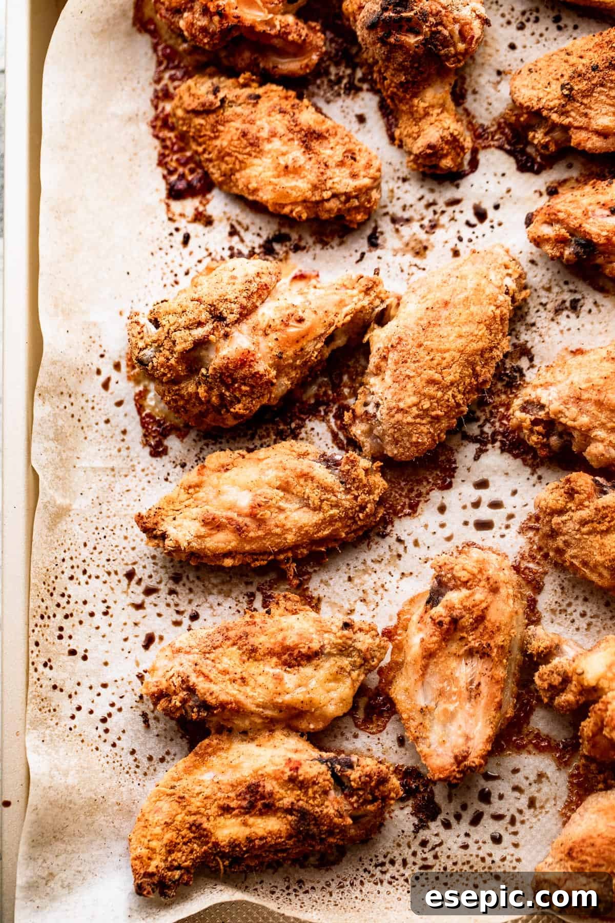An appetizing overhead shot of perfectly cooked hot wings, their golden-brown skin glistening, arranged neatly on a parchment-lined baking sheet. The wings appear crispy and ready for saucing, showcasing the successful baking process.