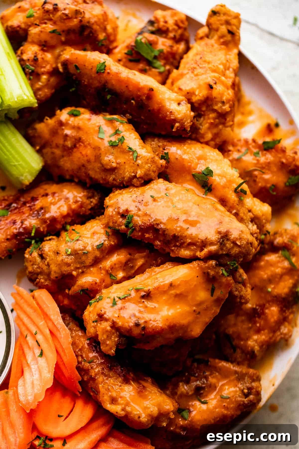 A beautiful close-up overhead shot of the Mango Habanero Hot Wings arranged on a white serving plate, highlighting their vibrant glaze and appealing texture. Accompanying the wings are fresh celery sticks and carrot sticks, providing a refreshing contrast to the spicy and sweet flavors.