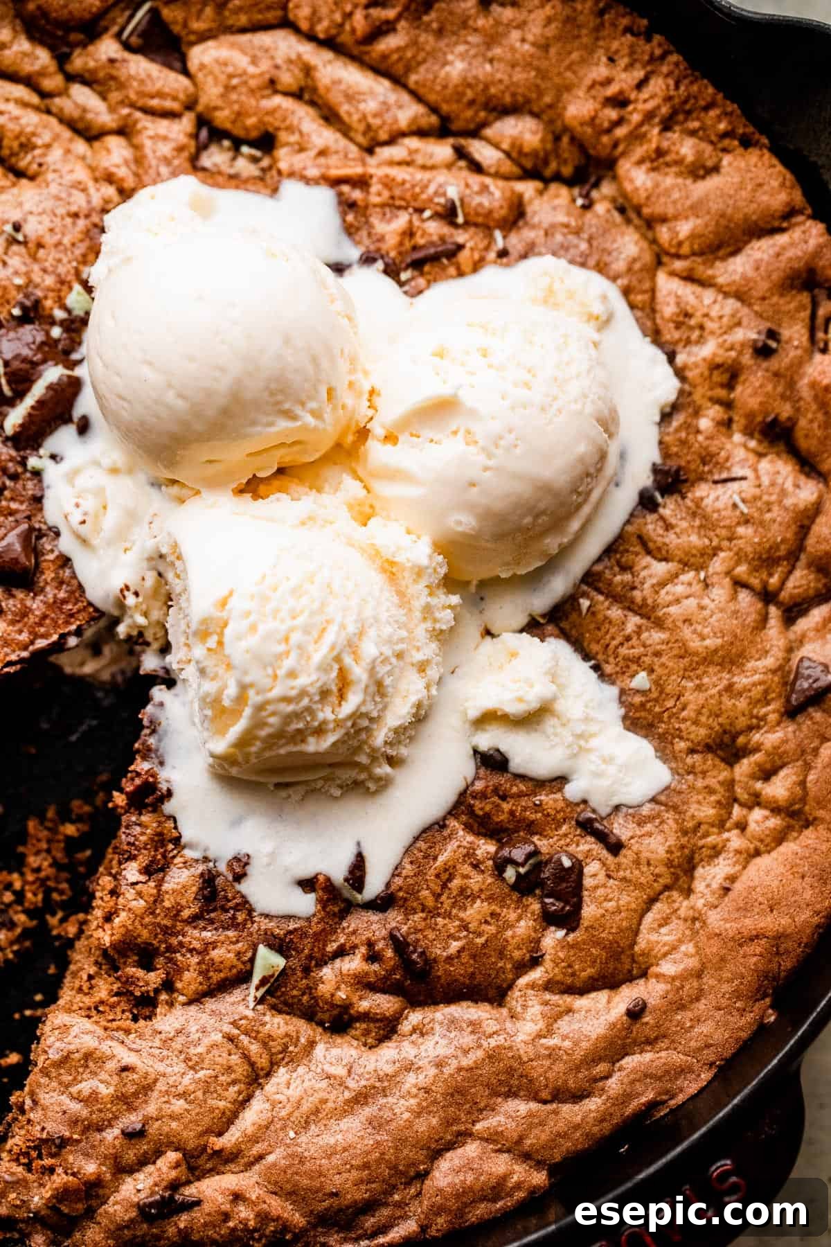 Close-up overhead shot of a large, warm mint chocolate skillet cookie served with three generous scoops of vanilla ice cream, creating a delightful contrast of colors and textures.