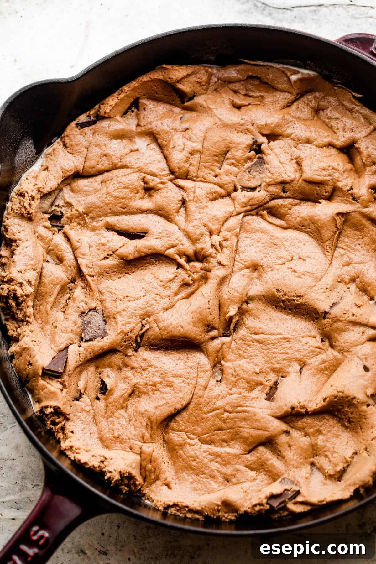 Raw mint chocolate cookie dough perfectly spread out into a greased cast iron skillet, ready for baking.